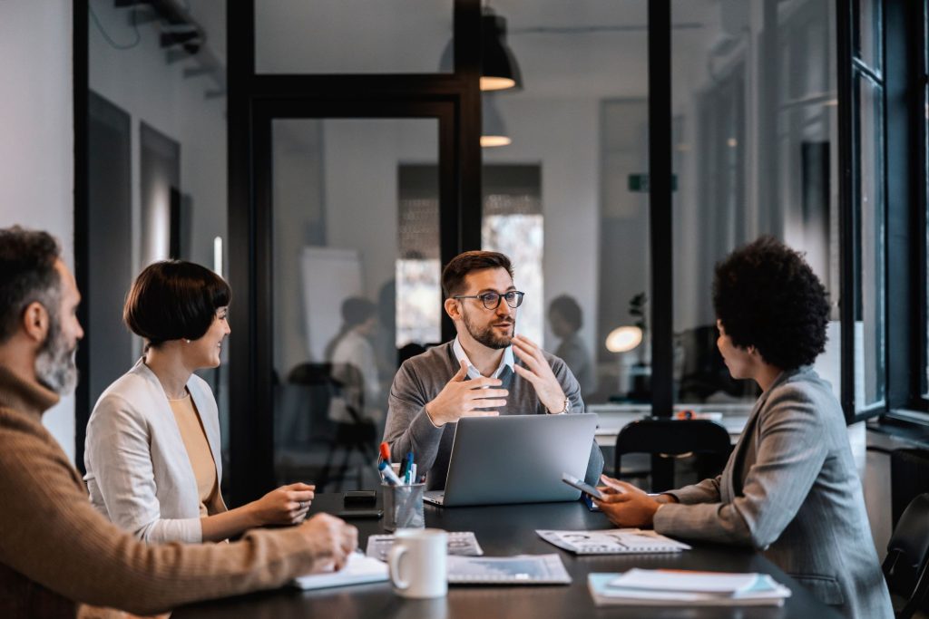 Dans une salle de réunion moderne et lumineuse, un consultant présente une solution à ses interlocuteurs autour d’une table. Cette image illustre l’esprit du Groupe Novances : un collectif d’experts engagés aux côtés des dirigeants pour simplifier leur quotidien, accompagner leurs décisions et donner du sens à leurs projets d’entreprise.