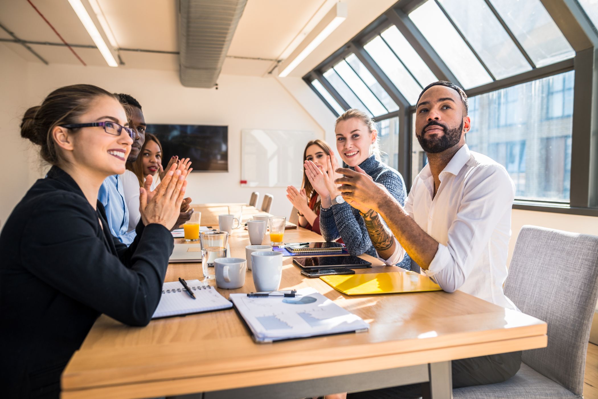 Groupe de collaborateurs en formation applaudissant et échangeant autour d’une table, illustrant le partage des savoirs et l’intégration de nouvelles équipes au sein du groupe Novances.