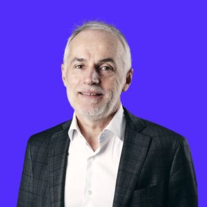 Portrait de Pascal Jourdan, président du Groupe Novances, en costume sombre et chemise claire, sur fond bleu uni.