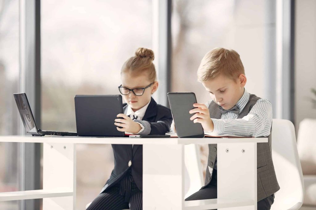 Enfants habillés en tenue professionnelle utilisant un ordinateur et une tablette, illustrant de manière humoristique l’idée de nouvelles générations prenant part à la stratégie de demain.